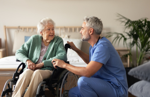 Mannlig helsepersonell prater med eldre kvinne i rullestol. Foto